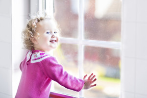 Beautiful little girl watching out of a window with autumn trees